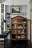 Antiker Geschirrschrank, umgeben von schwarz-weißer Fotosammlung an Kunststoff-Wellblech