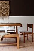 Rustic wooden table with bench and chairs in front of white-brown wall in dining room