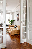Blick durch geöffnete Glasschiebetüren ins Altbau-Wohnzimmer auf bequemes Sofa und Bogenlampe