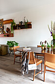 Dining room with wooden table, retro chairs and wall shelves with plants