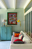 Gemütliches Sofa mit bunten Kissen und Vintage-Schrank in pastellgrünem Zimmer