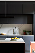 Modern, dark kitchen unit with marbled splashback and lemons on the counter