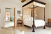 Four-poster bed with white curtains and striped wallpaper in the bedroom