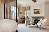 Four-poster bed and seating area in the bedroom with fireplace and striped wallpaper