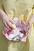 Woman with yellow dress, basket with colourful Easter eggs and cloth with floral pattern