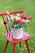 Frühlingsblumenarrangement auf rotem Stuhl im Garten