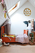 Children's room with orange-colored bed, toys and sloping ceiling