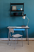 Vintage Schreibtisch mit Stuhl, darüber Regal an blauer Wand