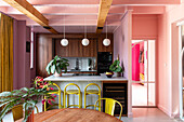 Open-plan kitchen in shades of pink, with yellow bar stools and wooden elements