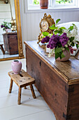 Wooden chest with bouquet of lilacs, mirror with gold frame in the background