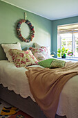 Bed with bedspread and floral cushions in bedroom with wreath decoration