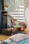 Chair under white staircase, fireplace and basket with firewood