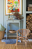 Console table with lamp and picture, rattan chair, wood storage for fireplace
