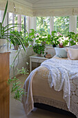 Bed with lace duvet and pillows, white bedside table and green houseplants