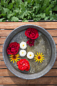 Metal bowl with flowers on a wooden table, surrounded by green plants