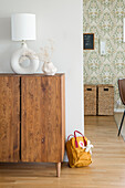 Wooden dresser with dried flowers and lamp, patterned wallpaper in the background