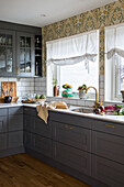 Kitchen with grey cupboards and floral wallpaper above the sink area