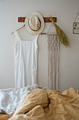 Weißes Sommerkleid und Hut an Garderobenleiste aus Holz