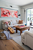 Wohnzimmer mit beigem Sofa, Couchtisch, abstraktem Wandbild und Gitarre