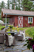 Terrassenecke mit Rattanmöbeln, rotes Landhaus im Sommer