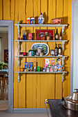 Wall shelves with collector's items in kitchen on yellow wooden wall