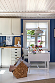 Country kitchen with blue walls and white cupboards, folding table in front of window