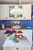 Küche mit blauer Wandverkleidung, weißen Möbeln und einer weißen Hängelampe