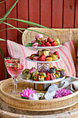 Etagere mit Erdbeeren und Macarons, Weingläser und Blüten auf Rattantablett