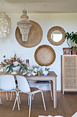 Dining area with rattan wall decoration and white chairs in naturally lit room