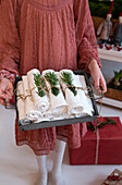 Frau präsentiert gerollte Servietten mit Rosmarinzweigen auf Metalltablett