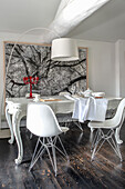 White dining table with curved legs and white Eames chairs in front of a large tree photo