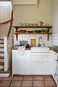 Small country-style kitchen with wooden shelves and terracotta tiles