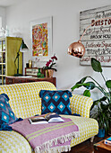 Gemusterte gelbe Couch mit Decke, Kunstwerke an der Wand, Vintage-Elementen und Zimmerpflanzen