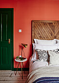Bedroom with orange-coloured wall, green door and rustic wooden headboard