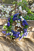 Spring wreath with grape hyacinths (Muscari) and daisies (Bellis perennis) and DIY pendant on wooden box