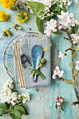 Napkin with letter made of string, tin spoon with grass decoration, between dandelion, lilac and apple blossom on cooling rack