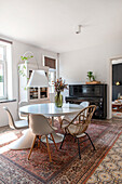 Dining room with round table, various chairs, patterned carpet and piano in the background