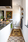 Long, narrow kitchen with patterned tiles and painting on the wall