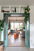 Open double door in turquoise to modern living room with herringbone parquet flooring and plants