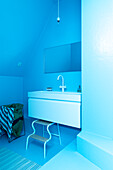 Minimalist blue bathroom with white washbasin and stool