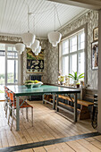 Dining room with green wooden table, orange-colored chairs and white pendant lights