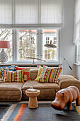 Living room with colorful ethnic print pillows and leather hippo in front of large windows