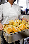 Bäckerin hält ein Blech mit frisch gebackenen Scones