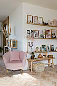 Helles Wohnzimmer mit rosafarbenem Sessel und Wandregalen mit Bilderrahmen