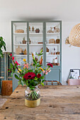 Bunter Blumenstrauß auf Holztisch vor mintfarbenen Vitrinenschrank im Wohnzimmer