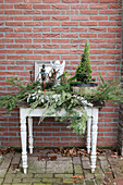White console table with winter decorations made of fir greenery in front of brick wall