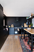 Black fitted kitchen with dark wall and oriental rug