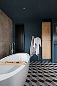 Modern bathroom with petrol-coloured walls, free-standing bath and geometric tile pattern