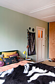 Bedroom with light green wall, bed with patterned textiles and yellow bedside lamp