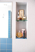 Perfume bottles and cosmetic products in wall niche in bathroom with blue tiles